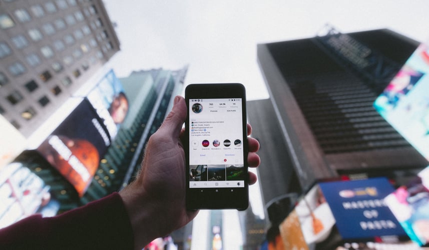 Man-holding-up-cell-phone-with-social-media-post-up-in-air-near-tall-buildings.