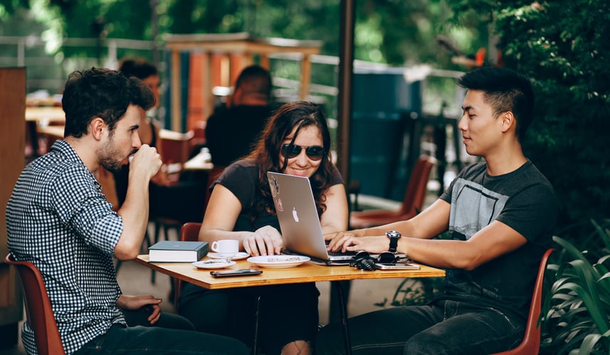 Three young adults having coffee while working on their laptops.