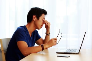 Young tired man sitting at the table with laptop at home