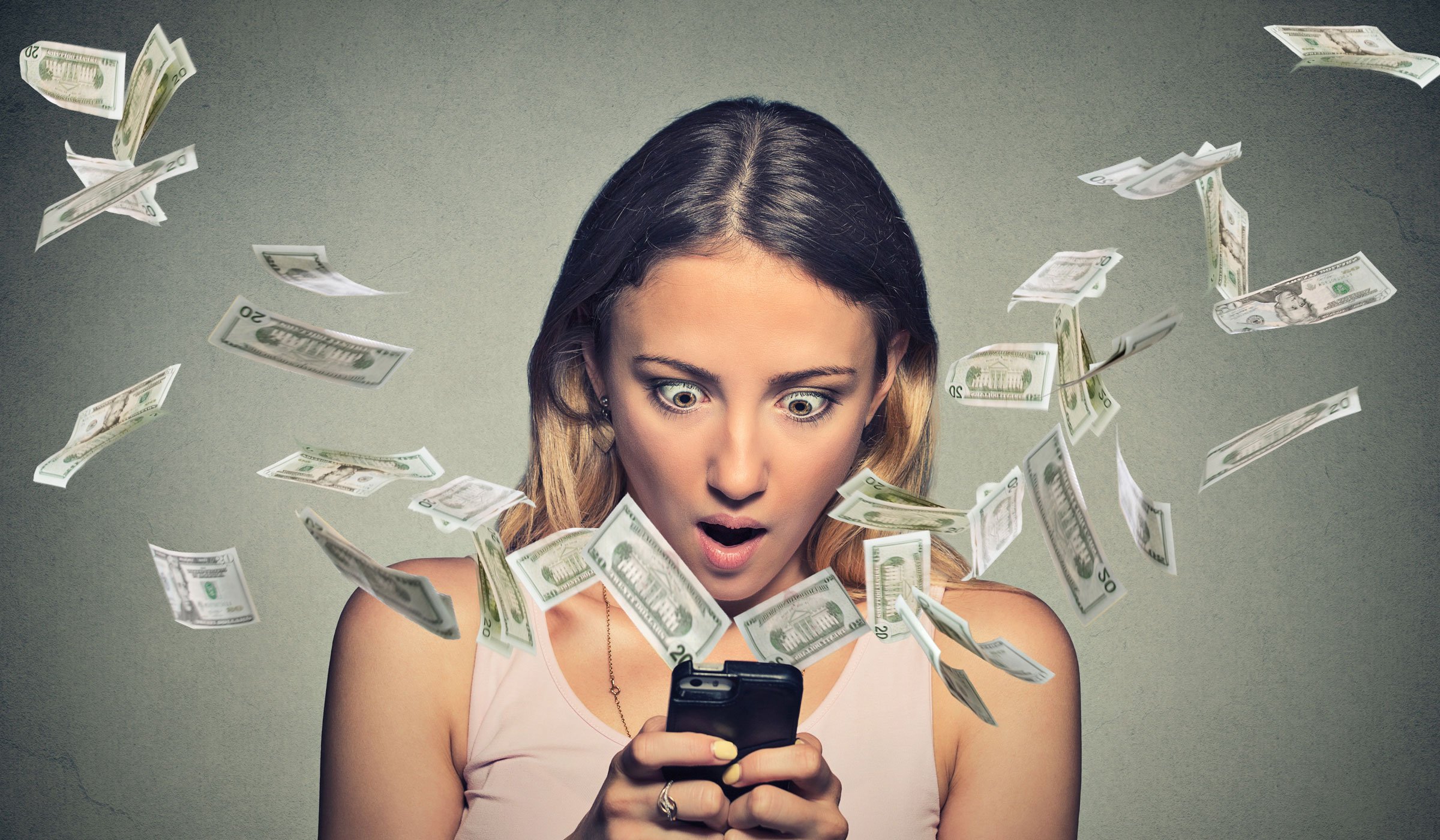 Woman watching her phone in shock as money flies out of it.